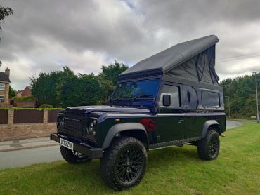 Black Land Rover Defender with raised roof parked on grass.