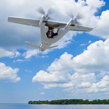 Small white seaplane flying over water under blue sky.