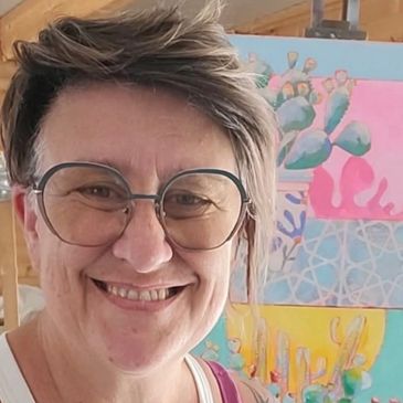 Mujer sonriente con gafas frente a pinturas de cactus.