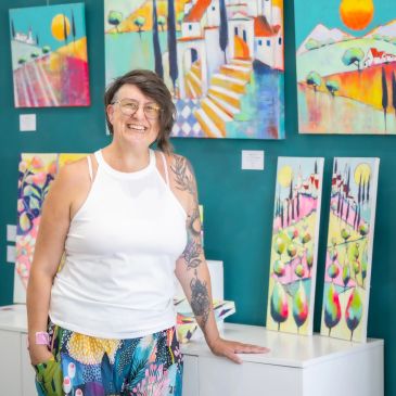 Mujer sonriente en una galería de arte con pinturas coloridas.