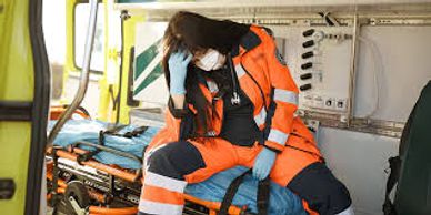 Tired paramedic sitting inside an ambulance, resting head on hand.