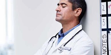 Doctor in white coat resting against wall, eyes closed.