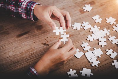 Hands assembling white puzzle pieces on a wooden table.