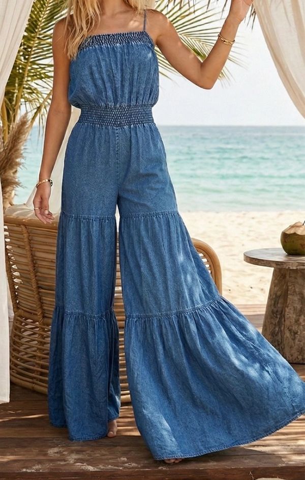 Woman wearing a blue denim jumpsuit by the beach under a canopy.