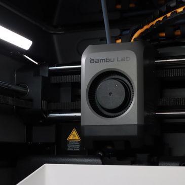 Close-up of a Bambu Lab 3D printer head with caution sign.