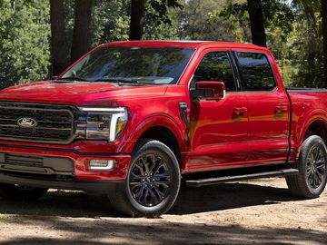 A red Ford pickup truck parked on a dirt path in a wooded area.