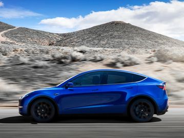 Blue Tesla SUV driving on a desert road under a clear sky.