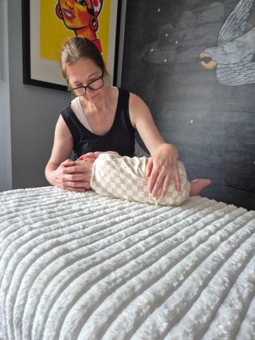 Woman gently holding a sleeping baby wrapped in a checkered blanket.