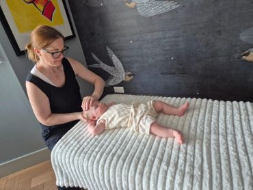 Woman gently massages a baby lying on a textured blanket.