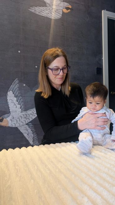 Woman in glasses holding a baby in a room with bird wall art.