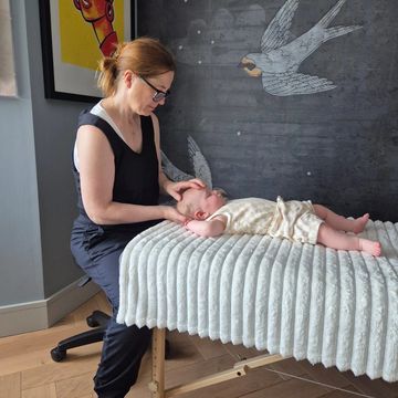 A woman gently massages a baby lying on a cushioned table.