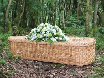 Wicker coffin with white flowers in a forest.
