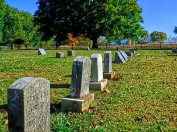 Old gravestones in a cemetery under clear blue sky.