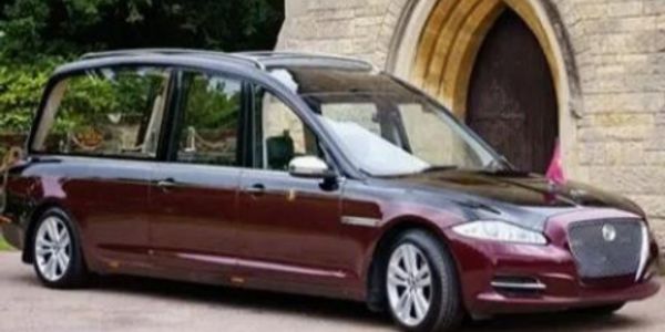 A hearse car parked near a stone building archway.