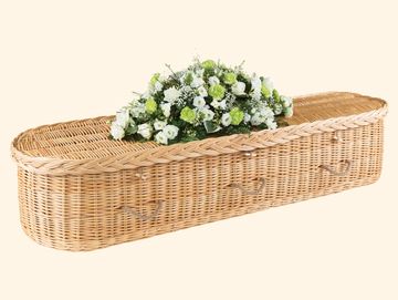 Wicker coffin with white and green floral arrangement.