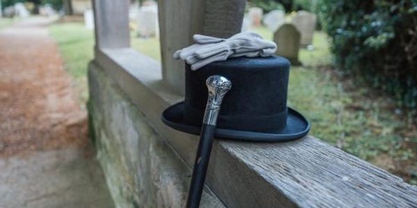 Black top hat, gloves, and cane on a wooden fence near a cemetery.