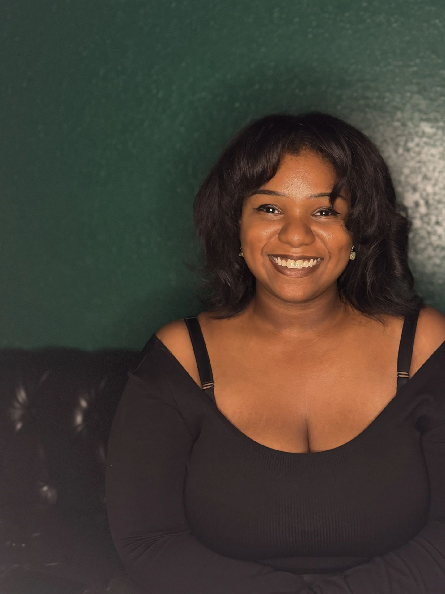 Smiling woman in a black top against a dark green background.