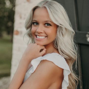 Smiling blonde woman in white dress posing outdoors.