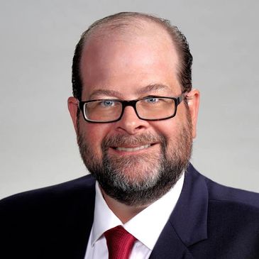 Portrait of a smiling man in glasses and a suit with a red tie.