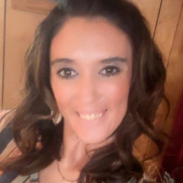 Woman with long curly hair smiling indoors.