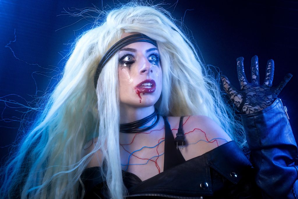 Woman with dramatic makeup and long blonde hair in a dark, electric-themed setting.