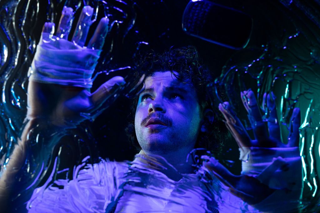 Man with painted hands touching glass under blue light.