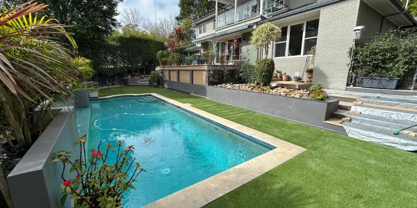 Modern backyard pool with artificial grass and plants.
