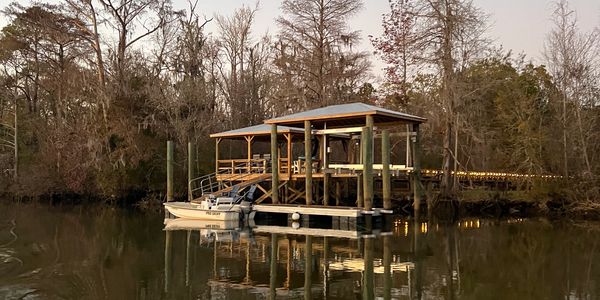 A small dock with a boat on calm water surrounded by leafless trees.