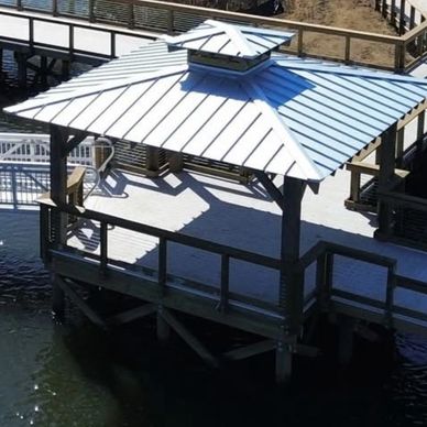 Wooden gazebo with metal roof over water on a sunny day.