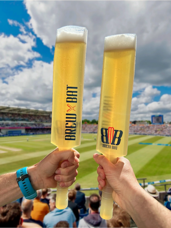 Two hands holding cricket bat-shaped beer glasses at a stadium.