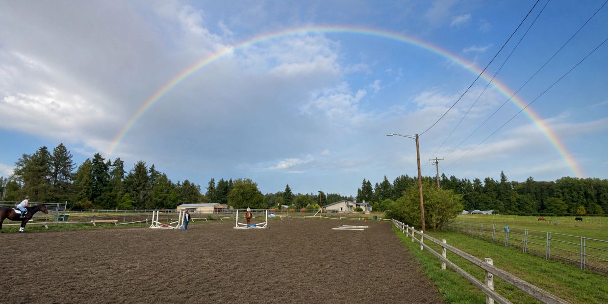 Rainbow over an equestrian field with riders and horses.