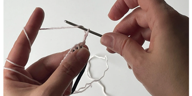 Hands crocheting with white yarn and a metal hook.