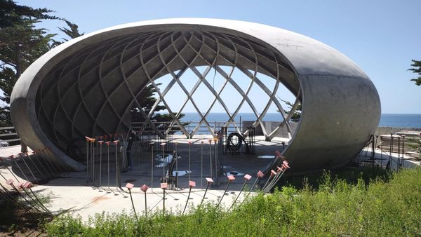 A modern, oval-shaped concrete structure with lattice design near the coast.