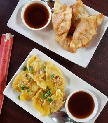 Two plates of dumplings with dipping sauce and chopsticks on the side.
