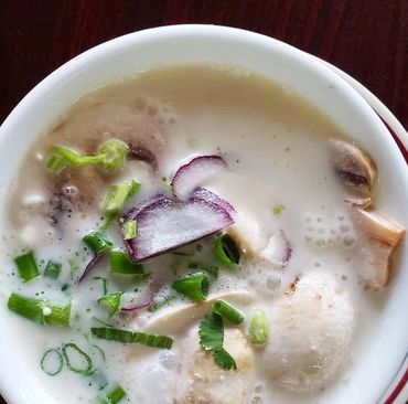 A bowl of creamy coconut soup garnished with mushrooms, onions, and spring onions.