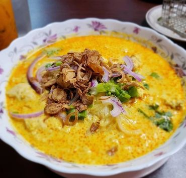 A bowl of creamy yellow soup garnished with fried onions, green onions, and purple onion slices.