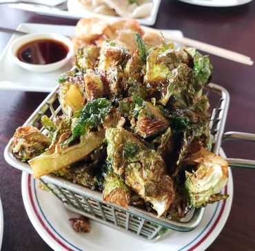 Crispy fried Brussels sprouts served in a mini fryer basket with dipping sauce in the background.