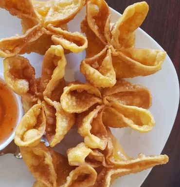 Golden fried wontons served with a side of dipping sauce on a white plate.