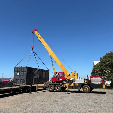Yellow crane lifting a black container at a worksite.