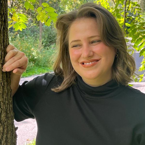 Smiling woman in black shirt leaning on tree outdoors.