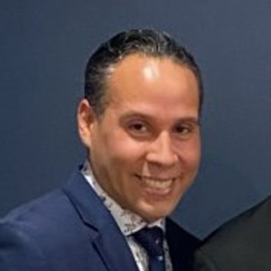 A smiling man with a printed shirt and blue blazer