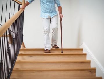 Person using a cane while walking down wooden stairs.