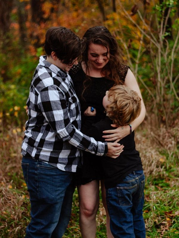 Three people sharing a warm group hug outdoors in autumn.