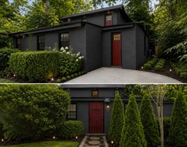 Modern black house with red doors and lush green landscaping.