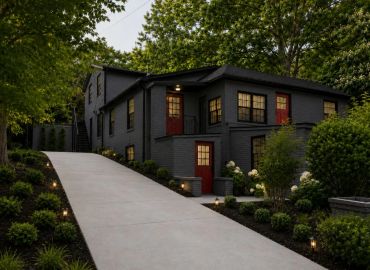 Modern black-painted house with red doors and a well-lit driveway.