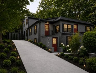 Modern black house with red door and lights on at dusk.
