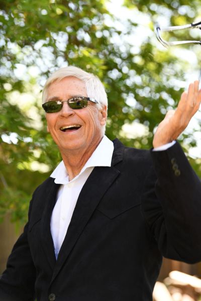 Smiling elderly man in sunglasses and a black suit outdoors.