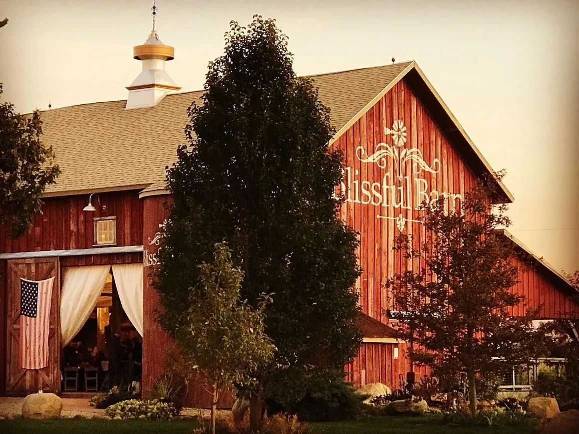 Rustic red barn with American flag and trees at sunset.