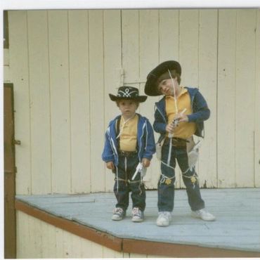 Two boys dressed as cowboys outside.