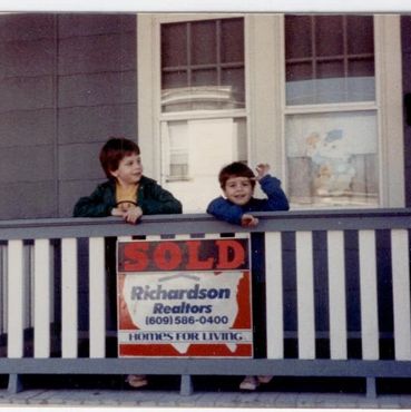 Children on a porch with a "Sold" sign.